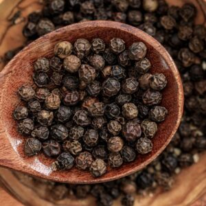 High-quality macro shot of black peppercorns in a wooden spoon on a bowl.